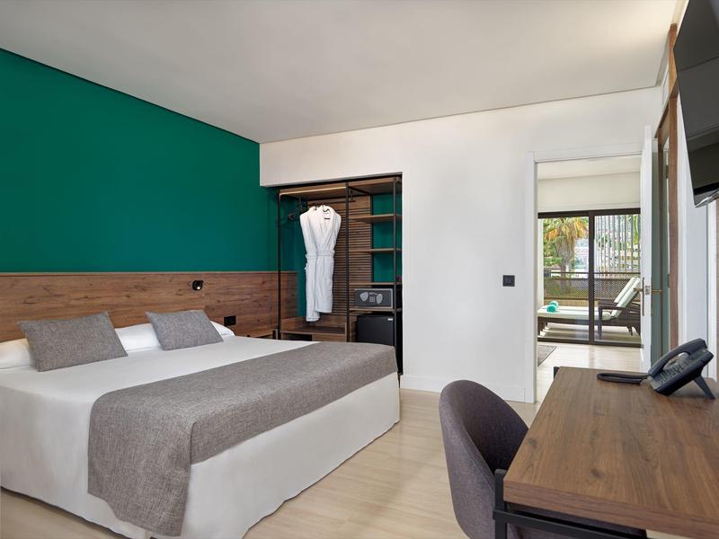 Camera d'hotel moderna con letto matrimoniale, cuscini grigi, scrivania in legno e armadio aperto.