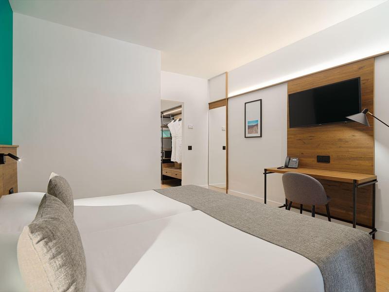 Camera d'hotel moderna con letto, TV a parete e scrivania minimalista.