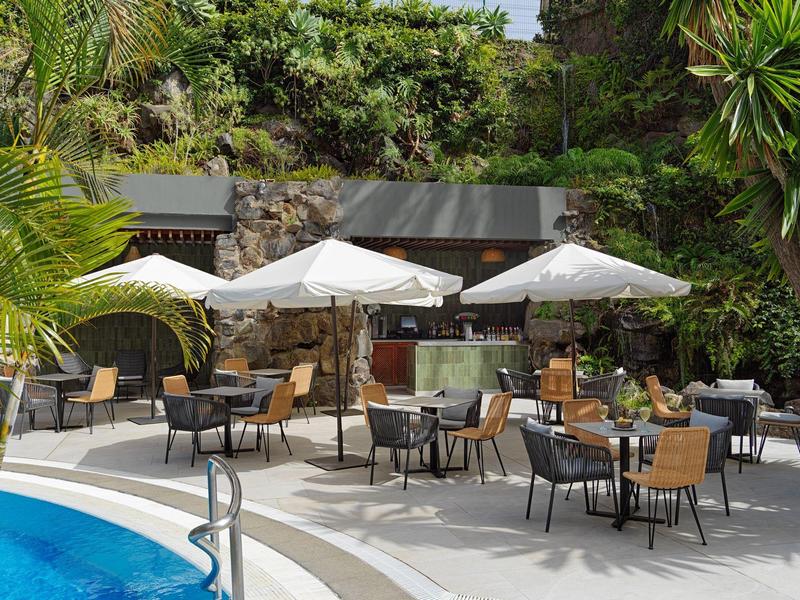 Terrazza con ombrelloni accanto a una piscina circondata da vegetazione tropicale.