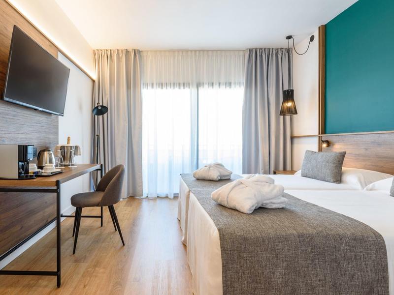 Camera d'hotel moderna con letto matrimoniale, TV, scrivania e ampia finestra luminosa.