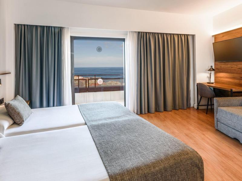 Camera d'hotel moderna con letti matrimoniali e finestra grande con vista mare.