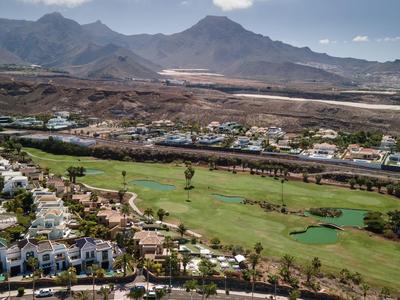 Grüne Golfanlage vor städtischem Gebiet mit Bergen im Hintergrund unter blauem Himmel.