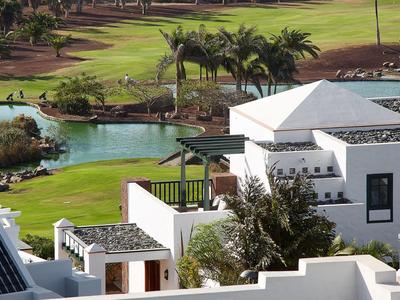 Biały budynek obok zielonego pola golfowego z palmami i stawem wodnym.