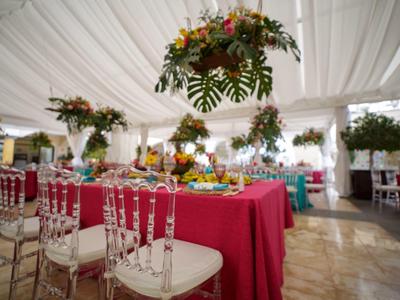 Festlich dekorierte Sitzordnung mit roten Tischdecken, Blumenarrangements und durchsichtigen Stühlen.