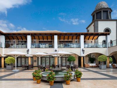 Dziedziniec hotelu z fontanną i otaczającymi balkonami pod niebieskim niebem.