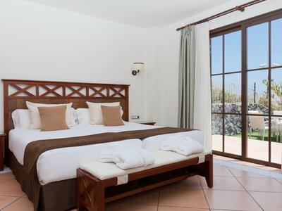 Gemütliches Schlafzimmer mit Holzmöbeln, großen Fenstern und hellem Fliesenboden.