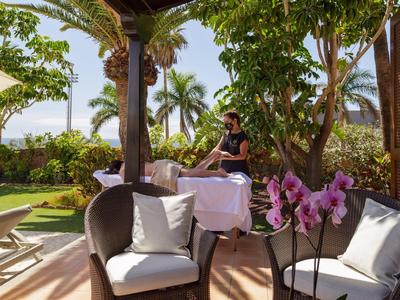 Terrassenbereich mit Stühlen, Tisch, Orchideen und einer Person in tropischem Garten.