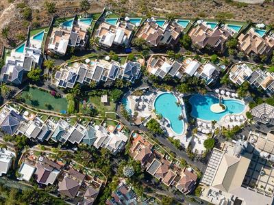 Luftaufnahme einer Wohnanlage mit weißen Häusern, grünen Gärten und einem blauen Pool in der Mitte.