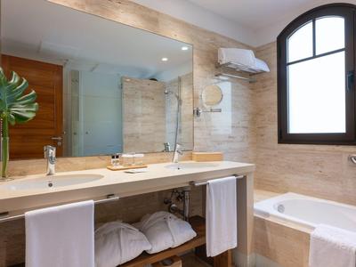 Moderne Badezimmer mit großem Spiegel, Badewanne, hellen Fliesen und Holzmöbeln.