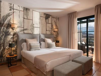 Helles Schlafzimmer mit großem Doppelbett, floralem Wandbild, Teppich und Balkon mit Blick.