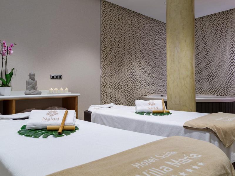 Modernes Massagestudio mit zwei Liegen, beige Decken und dekorativen Pflanzen.