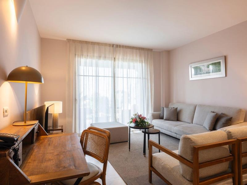 Helles Wohnzimmer mit grauem Sofa, Holzmöbeln, großem Fenster und warmem Licht.