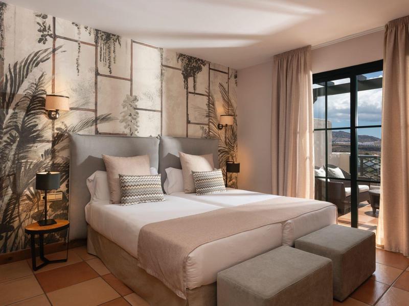 Helles Schlafzimmer mit großem Doppelbett, floralem Wandbild, Teppich und Balkon mit Blick.