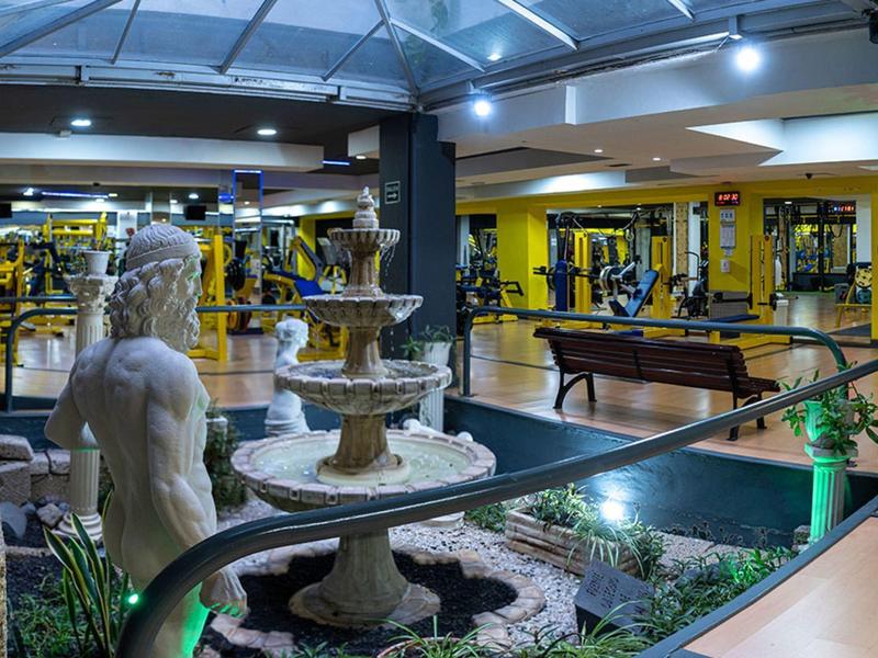 Innenraum eines Fitnessstudios mit Springbrunnen, Skulptur und zahlreichen Trainingsgeräten.