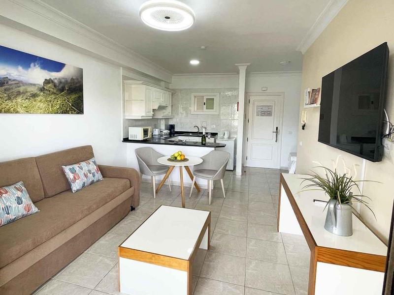 Moderne helle Wohnküche mit braunem Sofa, weißen Möbeln und Wandbild, offene Raumgestaltung.