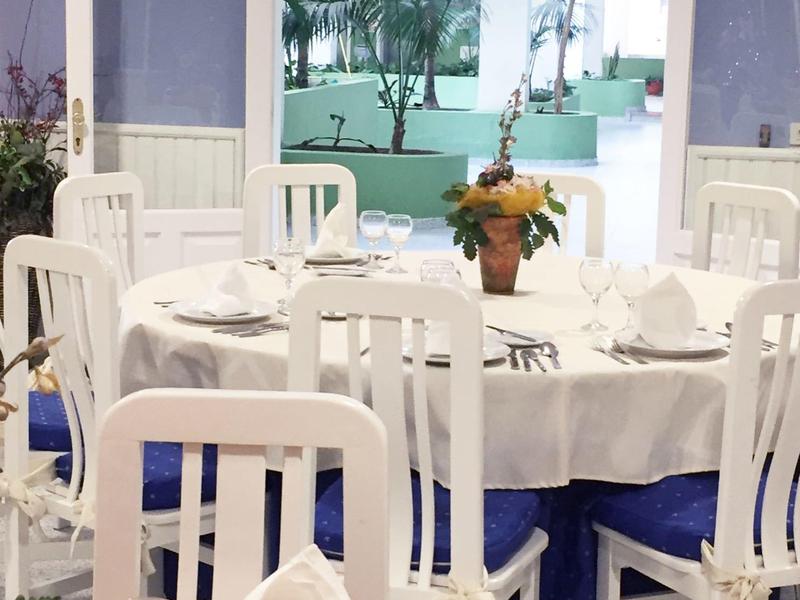 Hell eingerichteter Essraum mit rundem Tisch, weißen Stühlen und Blick auf grüne Pflanzen draußen.