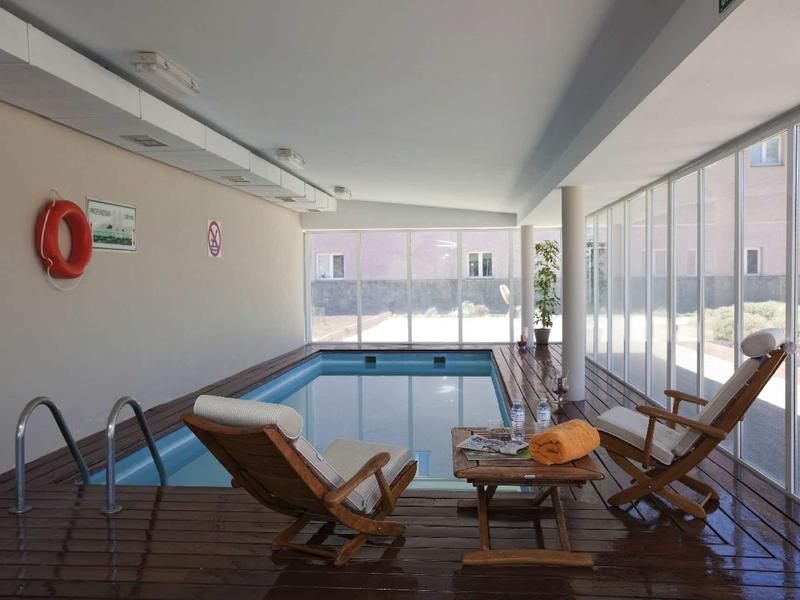 Indoor pool area with lounge chairs and large windows letting in natural light.