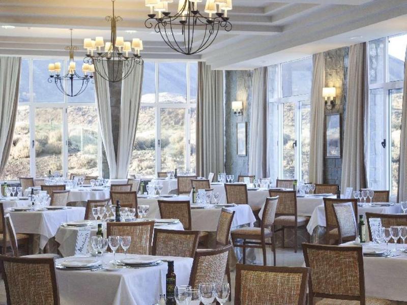 Elegant dining room with chandeliers, large windows, white tablecloths, and wooden chairs.