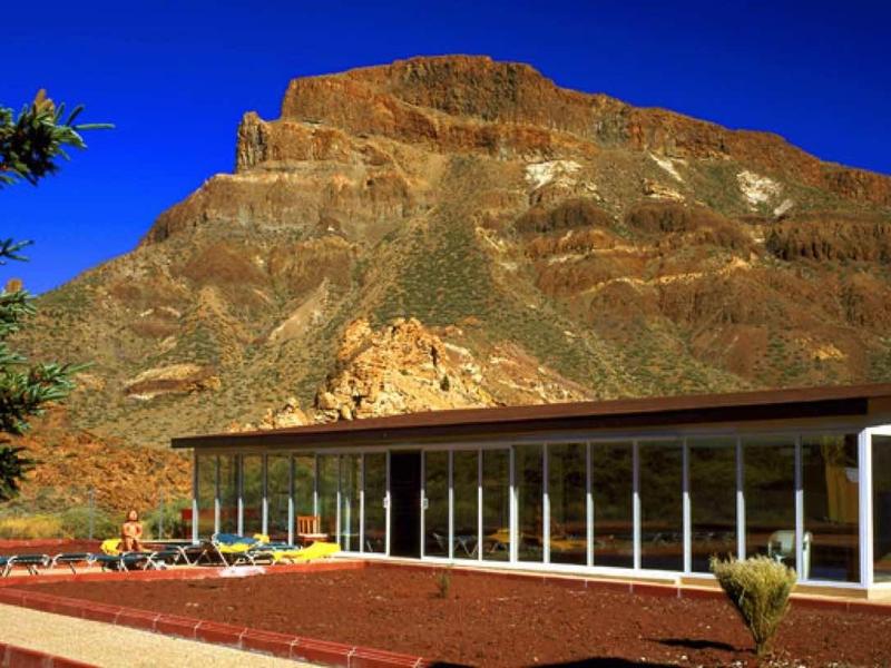 Modern glass building against a rocky mountain under a deep blue sky
