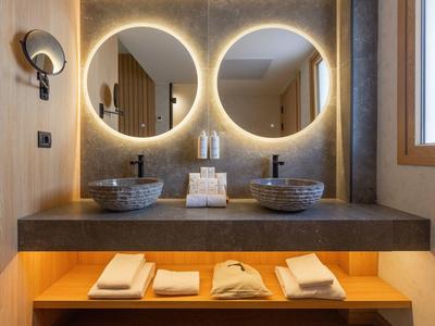 Nowoczesna łazienka z dwoma oświetlonymi okrągłymi lustrami i dwoma umywalkami na szarym blacie.