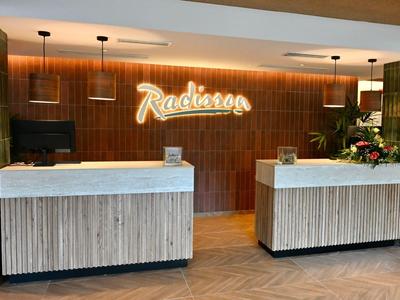 Nowoczesna recepcja hotelowa z dwoma ladami i podświetlonym logo na drewnianej ścianie.