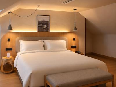 Modern hotelkamer met tweepersoonsbed, twee hanglampen en houten meubels in warm licht.