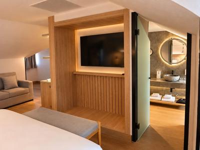 Modern hotelkamer met houten meubels, bank, grote tv en zicht op de badkamer.
