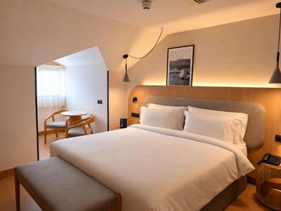 Modern hotelkamer met tweepersoonsbed, beige muren en zithoek bij het raam.