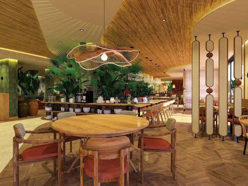 Nowoczesna przestrzeń lounge w hotelu z drewnianymi stołami, krzesłami i zielonymi ozdobami roślinnymi.