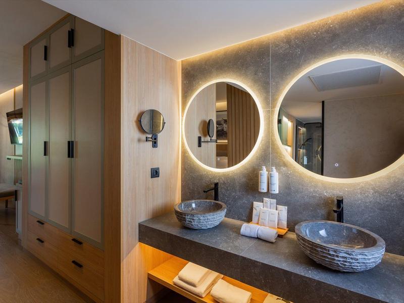 Nowoczesna łazienka hotelowa z podświetlanymi okrągłymi lustrami i dwoma kamiennymi umywalkami