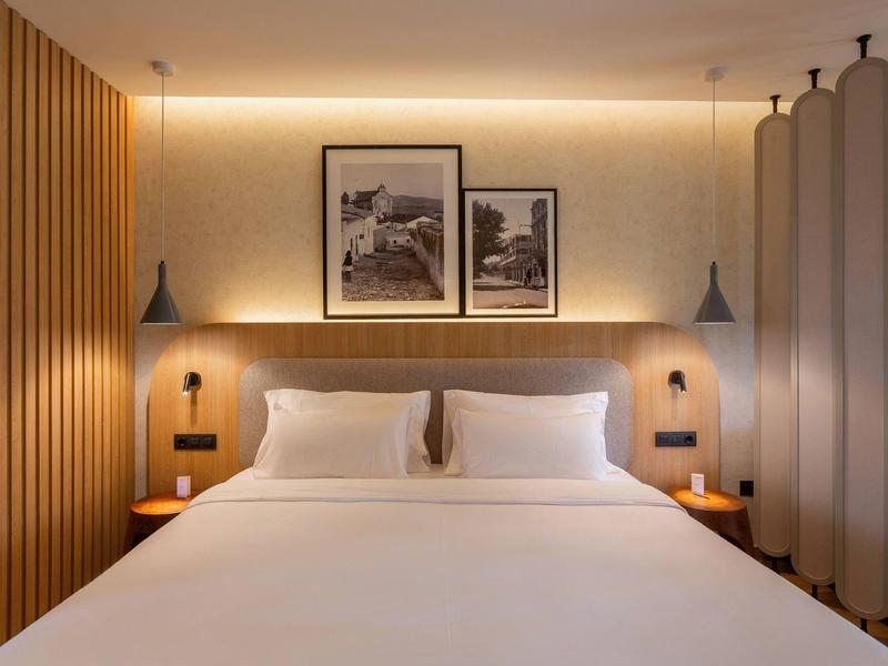 Nowoczesny pokój hotelowy z dużym łóżkiem, drewnianymi panelami i dwoma obrazami na ścianie.