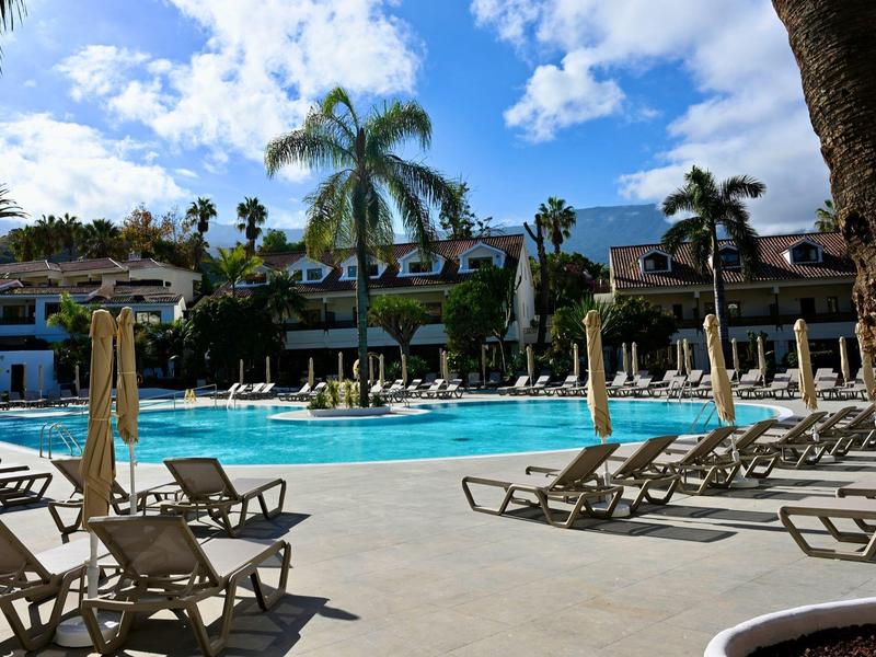 Basen hotelowy z leżakami, palmami i błękitnym niebem w miejscu wypoczynkowym.