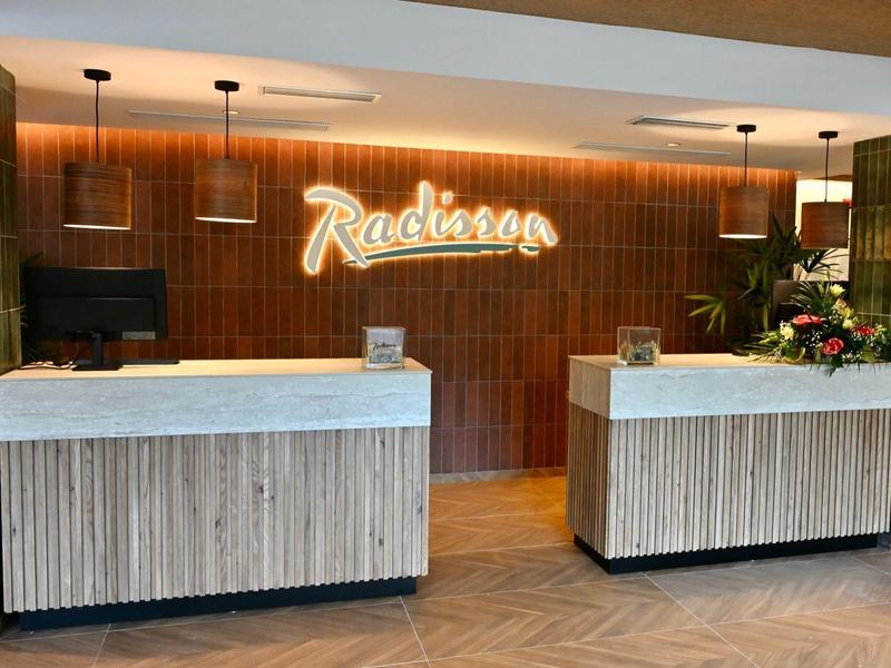 Nowoczesna recepcja hotelowa z dwoma ladami i podświetlonym logo na drewnianej ścianie.