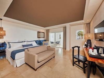 Moderní hotelový pokoj s manželskou postelí, lavičkou, stolem a přístupem na balkon nebo terasu.