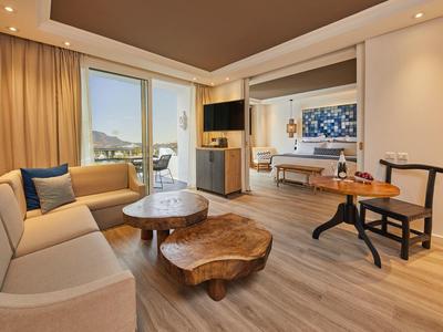 Habitación de hotel moderna con sofá, mesas de madera y balcón con vista al mar.