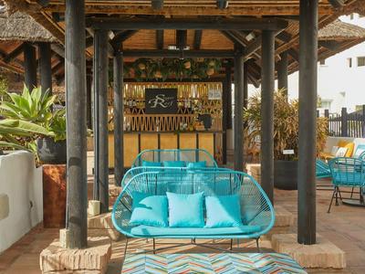 Área lounge abierta con asientos turquesa y bar bajo un techo de madera.