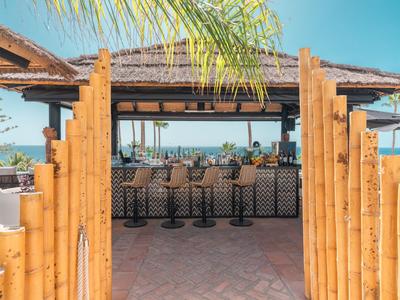 Otevřený venkovní bar s bambusovým vstupem a výhledem na oceán v pozadí.
