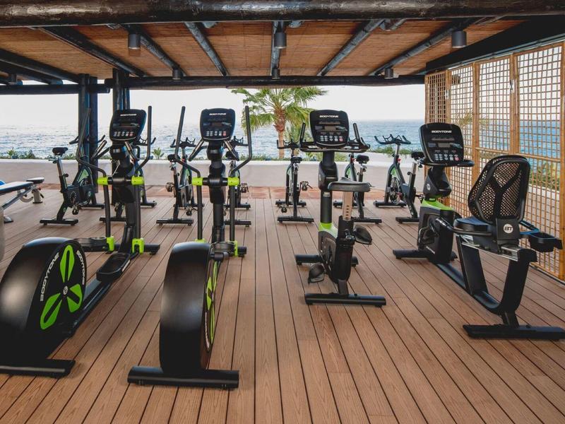 Gimnasio al aire libre con bicicletas estáticas y vistas al mar bajo un techo de madera.