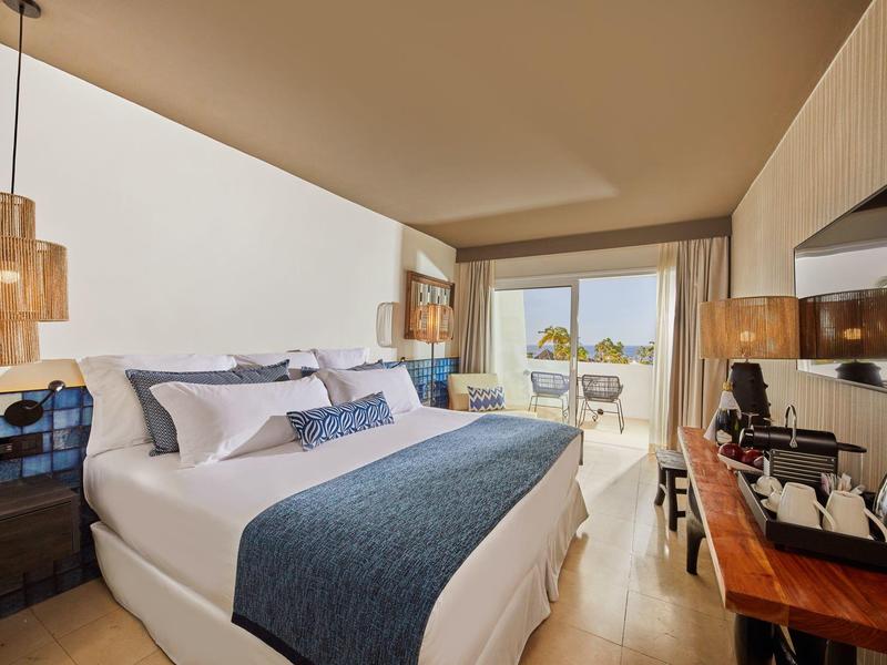 Habitación de hotel moderna con cama grande, escritorio, televisión y balcón con vista al exterior.