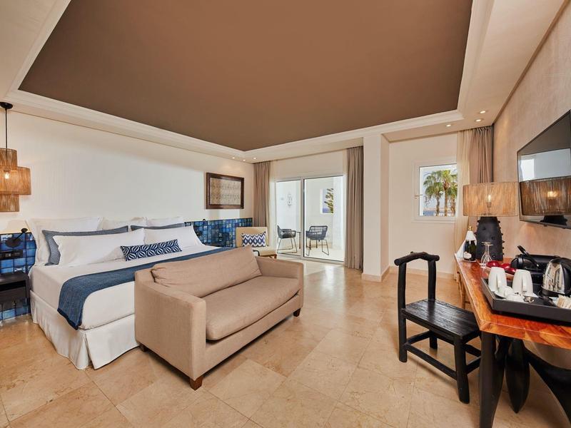 Habitación de hotel moderna con cama, sofá, escritorio y balcón con zona de estar.