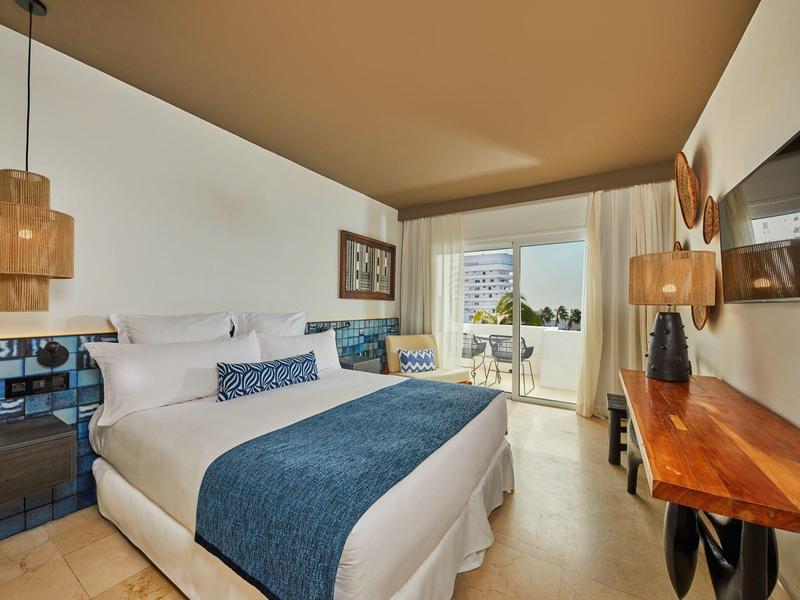 Habitación de hotel moderna con cama grande, muebles de madera y balcón con vistas al mar.