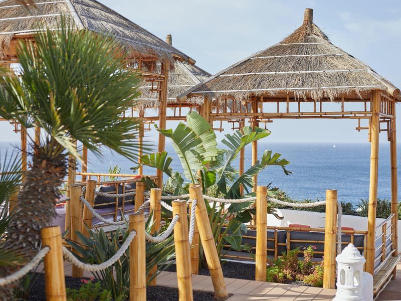 Chozas de bambú en la playa con vistas al mar y plantas tropicales.