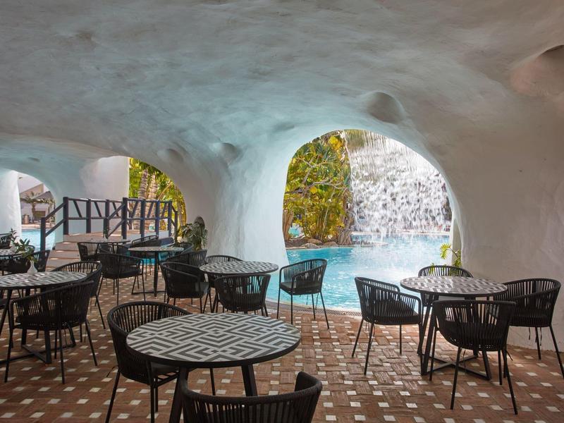 Zona exterior cubierta con arco redondeado, mesas y sillas frente a un entorno natural.