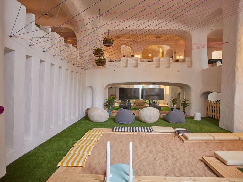 Área interior moderna con arenero, muro de escalada y césped verde para niños en un hotel.