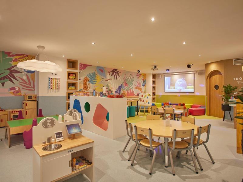 Sala de juegos infantil colorida con mesas, juguetes y paredes vibrantes en un hotel.