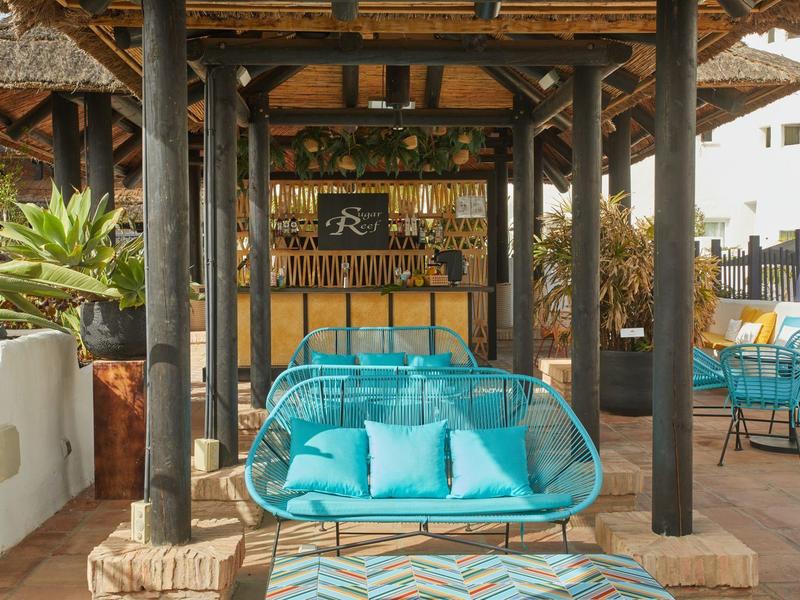 Área lounge abierta con asientos turquesa y bar bajo un techo de madera.