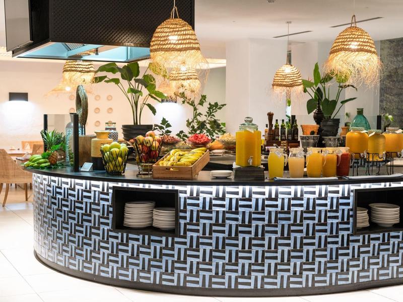 Bar moderno con frutas, bebidas e iluminación decorativa en una habitación luminosa.