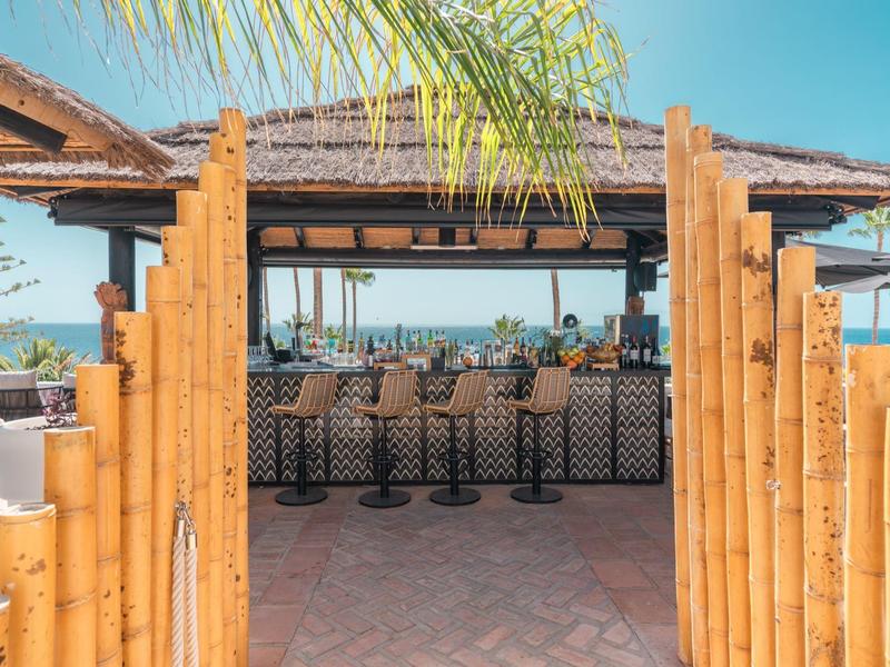 Lounge abierto con puerta de bambú y vista al mar bajo cielo azul.