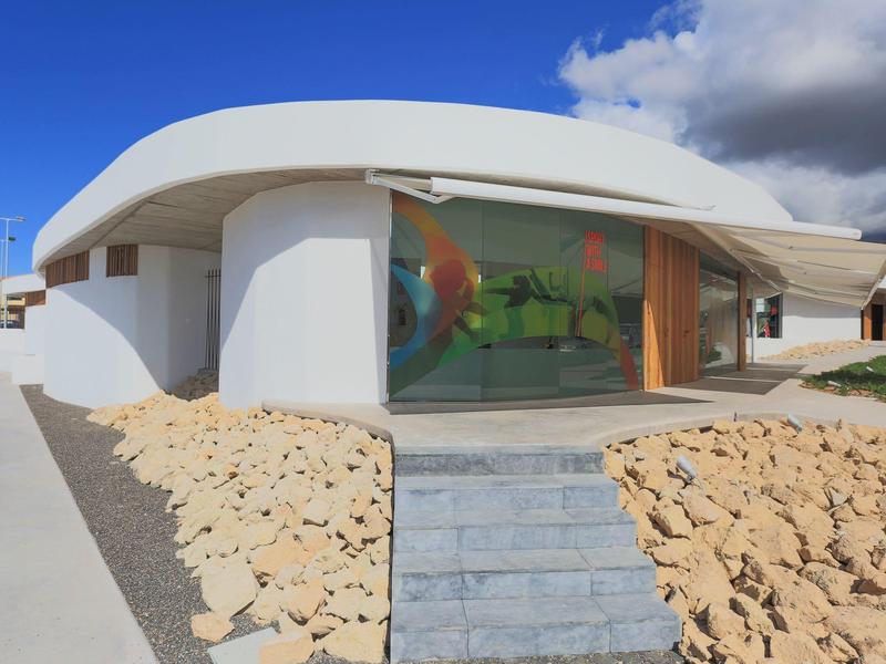 Maison blanche moderne avec grande façade vitrée et chemin en pierres devant l'entrée sous un ciel nuageux.