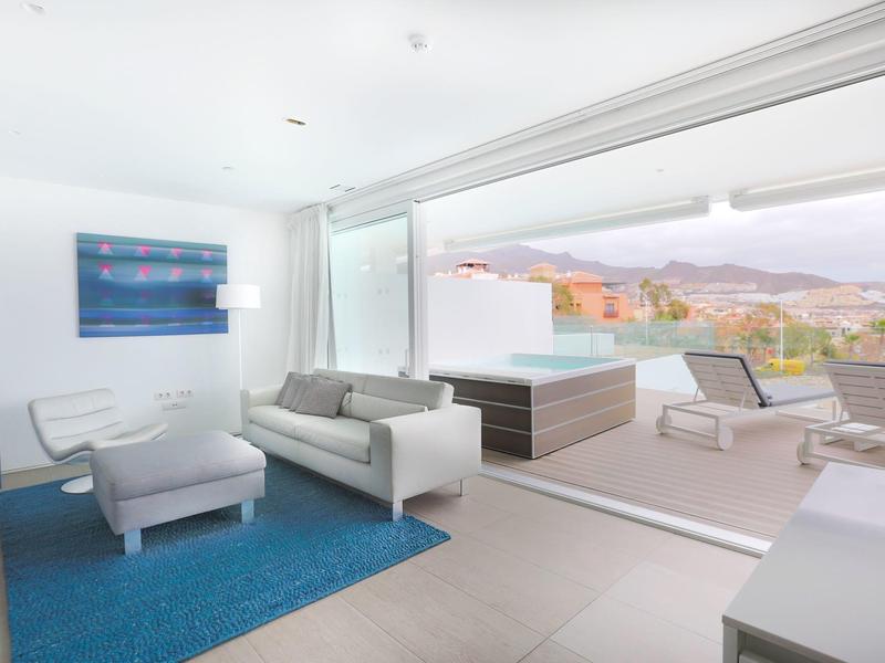 Terrasse moderne et lumineuse avec jacuzzi, espace lounge et vue sur les montagnes et la ville.